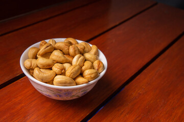 Close-up of roasted cashew nuts in a bowl on wooden table, healthy snack food rich in protein and nutrition