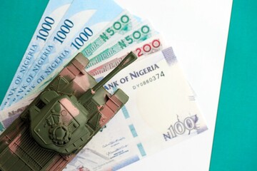 Nigerian naira currency money bills and toy tank on flag close up. The concept of army funds and weapons sales