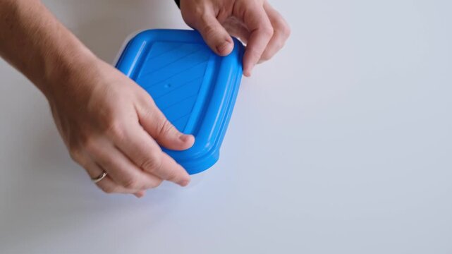 A man is closing the food container with blue plastic lid. The concept of convenient unbreakable tableware. Reusable tableware for storage and freeze. High quality 4K footage.