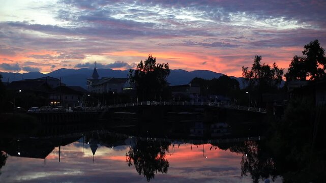The video background depicts the waterfront, with twilight sky illuminating the riverside community and the lights from houses, reflecting the rural lifestyle of Chanthaburi, Thailand.