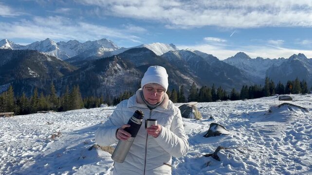 Portrait of a woman with thermos drinking hot beverage on the winter snowy mountains background