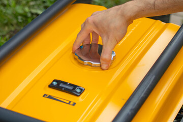 A close-up of a hand opening the lid of a yellow portable generator. The generator sits on a grassy surface, revealing its sturdy construction.