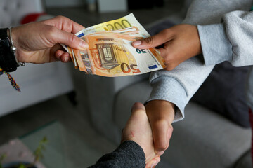 Two women closing a deal, handing over cash and shaking hands; one with light African American skin and the other Caucasian. Corruption
