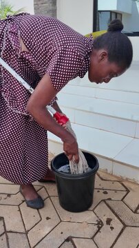 Lilongwe Malawi Africa, 01.12.2025. Video. African female worker squeezing water from mop into a bucket  after cleaning a patio of apartment.