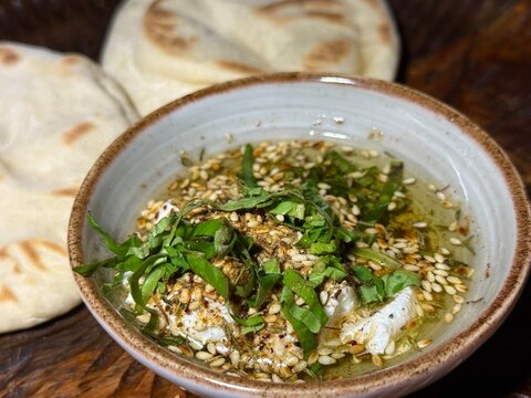 Close-up of a bowl of Labneh with olive oil, basil, Dukah and flatbreads