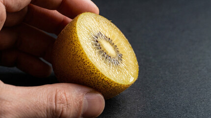 Hand holding a halved golden kiwi fruit against a dark background