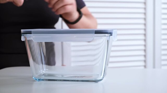 A man is closing the glass food container with a plastic lid with snaps. The concept of convenient bowl for safe. Reusable tableware for storage, baking and freeze. High quality 4K footage.