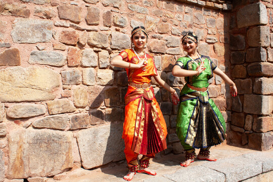 Two Teenage girls performing the Bharatanatyam Indian classical dance in front of a stone wall