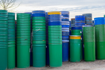 Many barrels are stacked in a storage area with some green and blue colors visible under the cloudy sky during the day