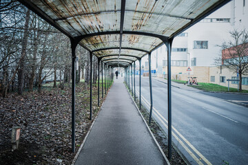 Abstract view of a single person seen in the distance, walking along a covered walkway on a hospital campus in the UK. Research and medical buildings can be seen.