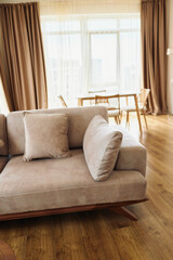 Sofa cushion livingroom hardwood curtains diningtable in a sunlit modern apartment interior, cozy neutral upholstery on wooden floor with minimalist dining area and soft natural light.