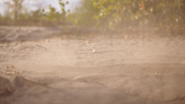 closeup tire kicking up dust over textured sand surface, tread biting into ground, granular particles swirling in sunlight while suspension responds, technical