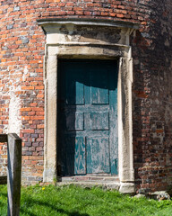 Historic brick doorway with a blue wooden door surrounded by lush green grass in a sunny landscape