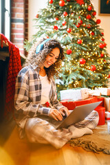 Cheerful woman with laptop and New Year's gifts is shopping online. A beautiful woman is having fun...