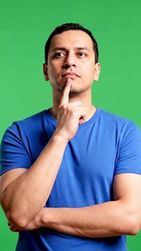 A man on a green screen, the video slowly zooms in on the man, who seems to be thinking about something with his index finger on his chin, Generative AI