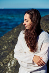 Fototapeta premium Young woman in white sweater near Baltic Sea on sunny day