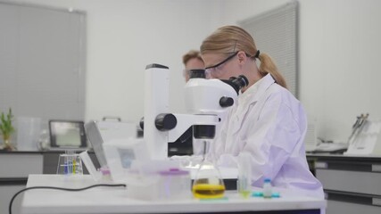Scientist conducts research using microscope in modern lab setting with colleagues present