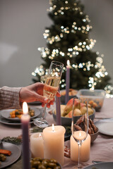 Pouring champagne at Christmas dinner table with candles and bokeh Christmas tree lights
