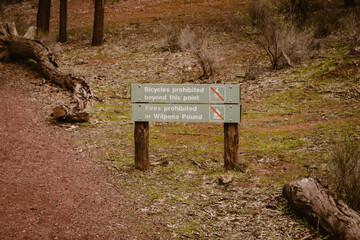 Wooden information board with symbols about bicycles and fires are prohibited along the walking path outdoor in the forest of Wilpena Pound in the Outback of Australia.