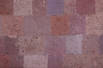 Background, texture of a wall lined with tiles made of pink tuff natural stone