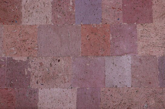 Background, texture of a wall lined with tiles made of pink tuff natural stone