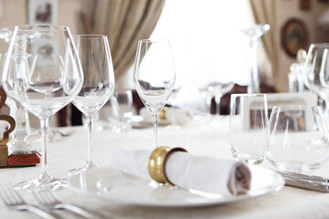 Festive table setting. Wine glasses and plates on the table. A white tablecloth. A cotton serving napkin with a yellow metal ring. The concept of the holiday.