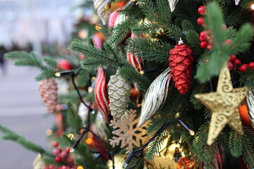 A branch of a Christmas tree with decorations: a gold star, a silver figurine, a red cone and other...