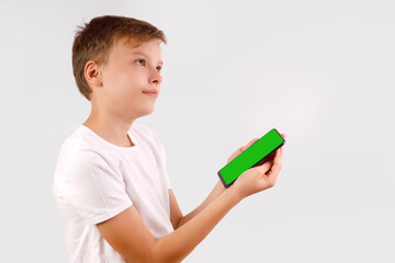 Side view of a young boy in a white t-shirt, holding a black smartphone horizontally with a bright green screen for easy content replacement