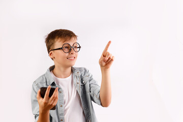 A happy boy wearing round, dark-rimmed glasses and a denim shirt, smiling and pointing his finger upwards to an imaginary screen