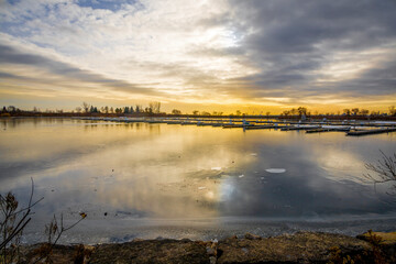 Fototapeta premium A serene winter sunset at Sam Smith Park in Etobicoke, Ontario, capturing a tranquil reflection over the icy waters.