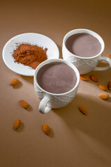 Cups of hot chocolate with cocoa powder and almonds on a simple background in a cozy setting