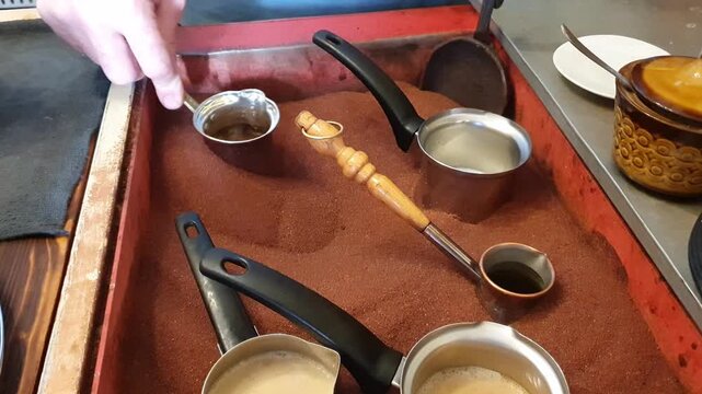 An authentic Eastern coffee-making process: a barista brews a fragrant drink in a copper Turk on hot sand, conveying the centuries-old traditions of coffee culture.