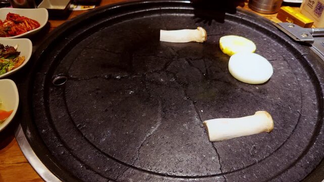 Round Grill Plate With Mushrooms and Onion Heated Before Cooking While Hand Places Food Using Tongs in Warm Light