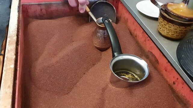 An authentic Eastern coffee-making process: the aromatic drink is brewed in a copper cezve over hot sand, symbolizing centuries-old traditions of hospitality and comfort. The video is perfect for illu