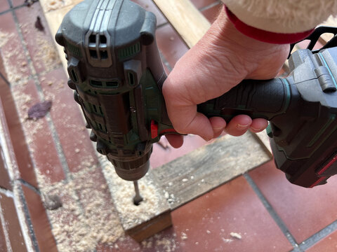 Proceso de perforaci&oacute;n de palets de madera con broca pala para crear una base estructural. Imagen mostrando trabajo visto desde lateral superior. Mano sujeta taladro.