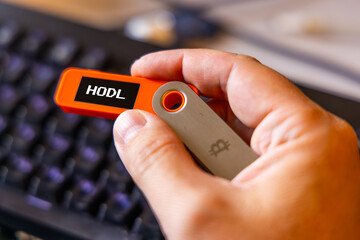 hardware Bitcoin wallet held in white hand with message Hodl on screen