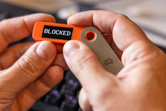 hardware Bitcoin wallet held in white hands with Blocked message on screen