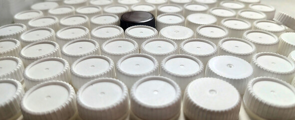 A field densely packed with white plastic bottle caps, with one dark brown black cap standing out in the center and creating a contrasting pattern.