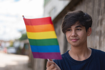 Teenaged boy wears rainbow wristband and holding rainbow flags, lgbtqai symbol, in front of wall, concept for calling out all people to respect human rights of lgbtqai people around the world.
