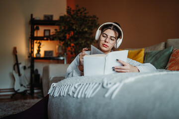 Young woman relaxing reading book wearing headphones