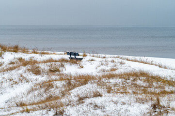 Empty bench on snowy dune overlooking frozen Baltic Sea in Latvia.