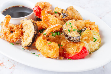 Shrimp and vegetable tempura, served with dipping sauce, on a white plate