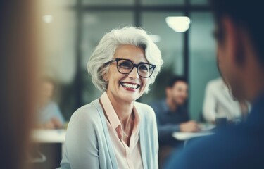 Smiling senior woman engages in conversation with colleagues in modern office environment showcasing teamwork and camaraderie