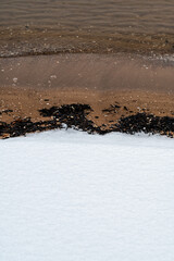 Snow-covered sand meeting Baltic Sea creating natural abstract composition