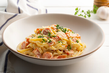 Fettuccine pasta with creamy carbonara sauce with pork sausage and bacon in a plate.
