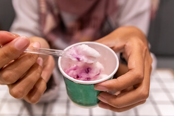 Hand holding a small cup of purple and white ice cream, scooped up with a clear plastic spoon