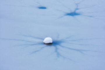 A close-up of a frozen surface with radial cracks and a snowball in the center. Abstract winter landscape, ice and snow texture