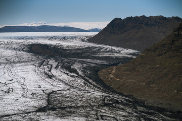 A wide aerial view of an Icelandic glacier winding between dark volcanic mountains