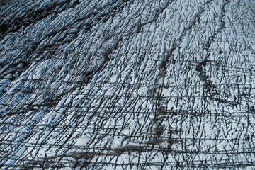 Aerial view of a glacier in Iceland showing striking natural patterns, cracks, and dark volcanic ash layers