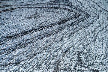 Aerial view of a glacier in Iceland showing striking natural patterns, cracks, and dark volcanic ash layers